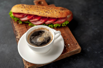coffee and a large panini sandwich with sausage and cheese in a white plate on a stone background with copy space for your text