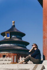brunette girl sitting on the steps by temple of heaven in China. Brunette girl enjoying chinese architecture while sitting on the steps and relaxing. Caucasian tourist taking a break from exploring