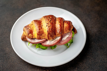 croissant sandwich with sausage and cheese in a white plate on a stone background with copy space for your text