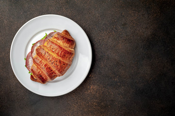 croissant sandwich with sausage and cheese in a white plate on a stone background with copy space for your text