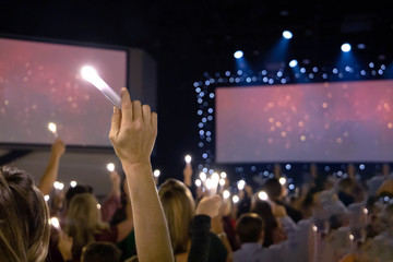 One single hand arm holding up a LED candle amongst a crowd of people at a candlight service concert with dual screens with copy space