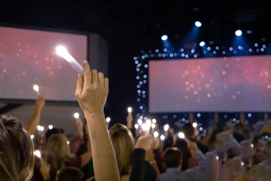 One Single Hand Arm Holding Up A LED Candle Amongst A Crowd Of People At A Candlight Service Concert With Dual Screens With Copy Space