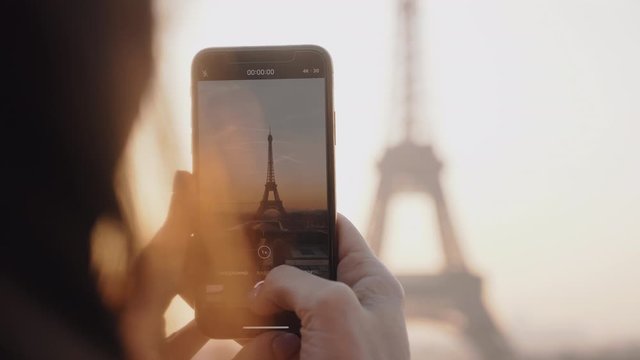 Close-up happy local blogger woman taking a video of epic sunset Paris Eiffel Tower sky panorama with phone slow motion.