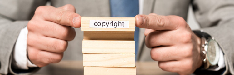 cropped view of businessman holding wooden block with copyright inscription isolated on grey