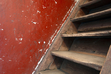 Old damaged brown wooden stairs and red wall leading to the attic, needs renovation