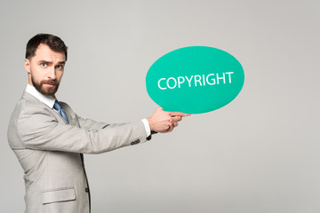 serious businessman holding thought bubble with copyright inscription isolated on grey