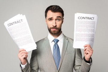 skeptical businessman holding contracts and looking at camera isolated on grey