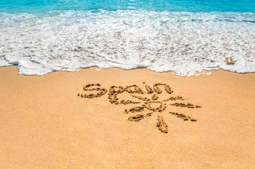 Hand written text Spain and sun symbol on the golden beach sand with coming waves