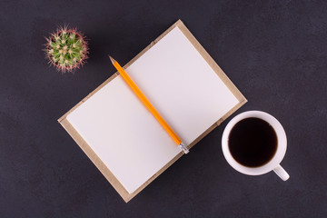 Open notebook, yellow pencil, cactus and a cup of black tea on a black table.