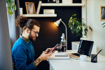 Young smiling attractive caucasian bearded graphic designer sitting at office  and using tablet.
