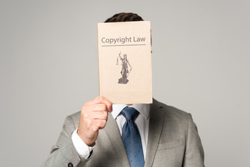 front view of lawyer obscuring face with copyright law book isolated on grey