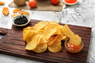 Tasty potato chips and caviar on table