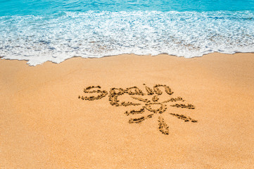 Hand written text Spain and sun symbol on the golden beach sand with coming wave