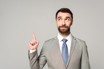 smiling businessman looking away while showing idea gesture isolated on grey