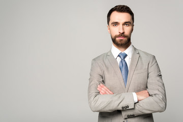 confident businessman standing with crossed arms and looking at camera isolated on grey