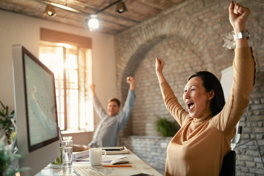 Happy Asian businesswoman screaming while reading good news on desktop PC.