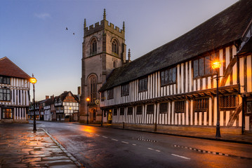 Stratford upon Avon, Guildhall and chapel with church. Street lights shine on timber framed buildings - obrazy, fototapety, plakaty