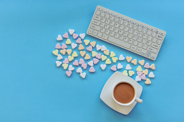 A cup of coffee, candies in a shape of hearts and keyboard on blue table. Top view, flat lay, copy space.