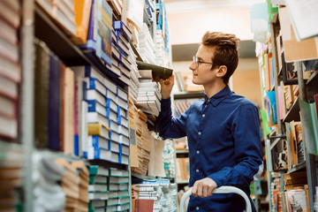 Male student looking for necessary book on numerous shelves in the library. Happy student finally...