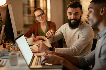 Happy entrepreneur cooperating with his colleague while working on laptop in the office.