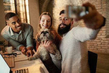 Happy freelancers having fun while taking selfie with a dog in the office.