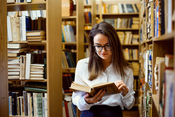 Female student in library reading a book, looking for materials to make research