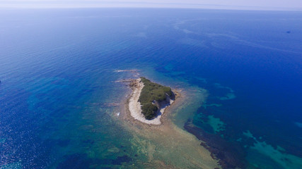 Fototapeta na wymiar Small island with green trees and rocky coast in the blue sea. Aerial view 