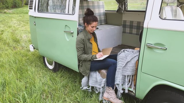 Woman sitting in camper and writing in daybook