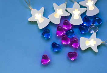 olored stones in the shape of hearts are blue, purple, white on a light blue background. Garland glowing in the shape of white angels.The concept of Valentine's day. The concept o