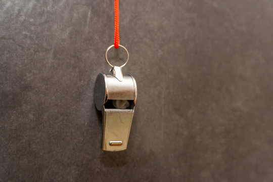 silberne Trillerpfeife hängt vor einer grauen Wand