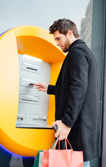 Young man with attractive beard takes money from an ATM.