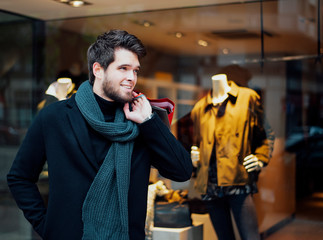 Attractive young man with a beard who has bags in one hand goes shopping in the city.