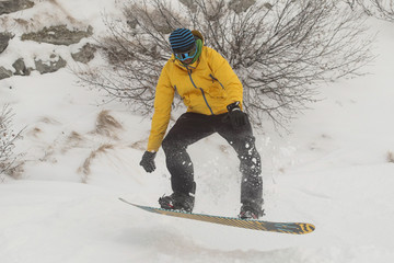 A snowboarder in snow going downhill amd jumping. Boarder with yellow clothing with black trousers...