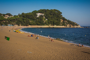 Fototapeta na wymiar Fenals beach in Lloret de Mar area in Spain. Late clear afternoon setting on a beach with blue ocean water on the mediterranean. Some people are seen on the beach.