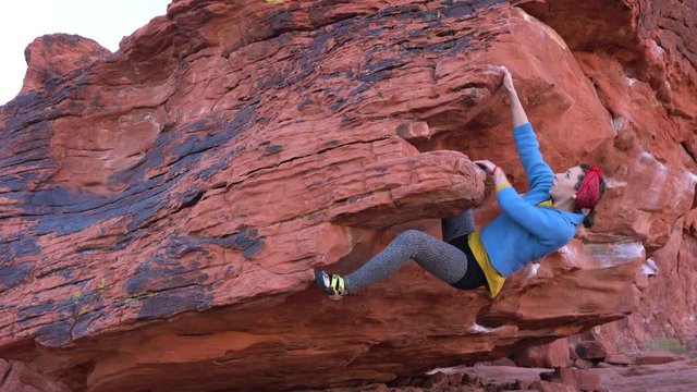 Athletic female rock climber doing hard moves on a overhanging boulder problem