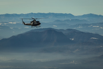 Army rescue helicopter hovering with side door open on the sky in front of a magnificent picturesque background with hills and mountain ridges. © Anze
