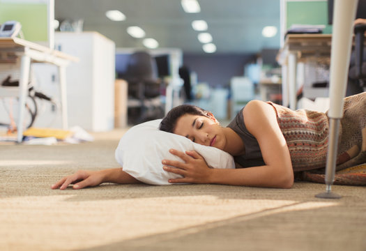 Businesswoman sleeping with pillow on office floor