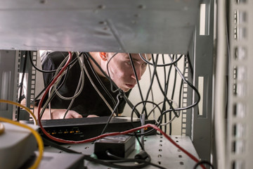 The specialist works in the server room of the data center. Technician is repairingcommunication cable line. A young man connects multimedia wires in the inside of the server rack.