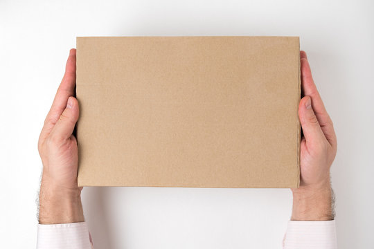 Rectangular cardboard box into men's hands on white background. Delivery service concept. Top view