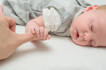 Baby holding finger of an adult. Care for the newborn. Closeup, white background