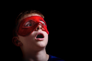 Boy in red carnival mask on black background. Portrait closeup isolated.