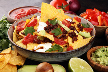 mexican nacho chips garnished with ground beef, guacamole, melted cheese, peppers and cilantro leaves in plate