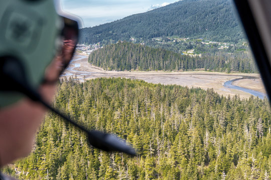 Flight seeing tour in Alaska. Sightseeing excursion on a helicopter over the national park. Beautiful rainforest and mountains. Lady is wearing a headphones and watching from the window of chopper. 