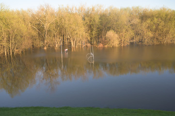 a football goal post, field, and forest is flooded with rain water one sunny spring afternoon