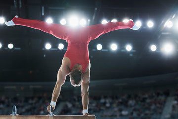 Male gymnast performing upside-down handstand on pommel horse