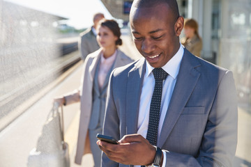 Businessman texting with cell phone on train station platform
