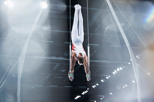 Male gymnast performing upside-down on gymnastics rings in arena