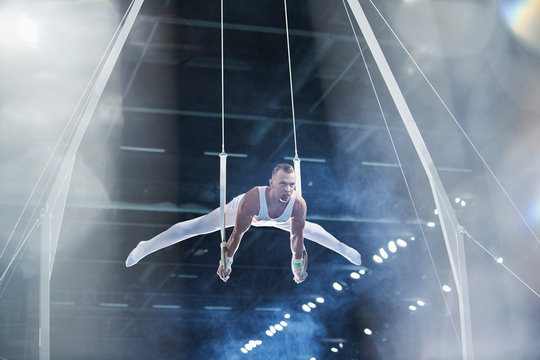 Male gymnast performing on gymnastics rings in arena