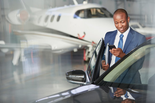 Businessman cell phone getting into car near corporate jet in hangar