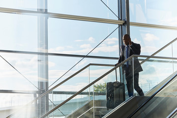 Businessman with suitcase talking on cell phone on airport escalator